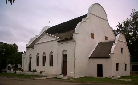 The Moravian mission church at Mamre &mdash; a whitewashed Cape Dutch building with a scrolled gable and thatched roof, gravestones in the churchyard beside it.