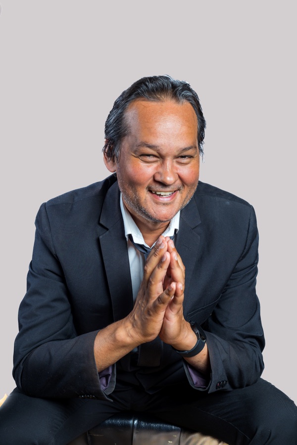 Studio portrait of Ramon Alexander in a dark suit, hands together, smiling.