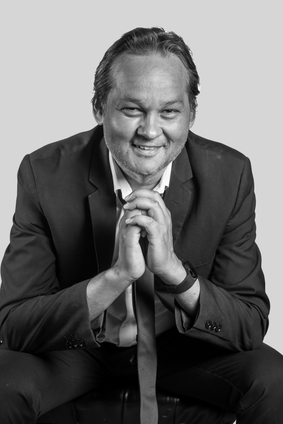 Black-and-white studio portrait of Ramon Alexander, seated in a dark suit with his hands clasped, looking to camera.